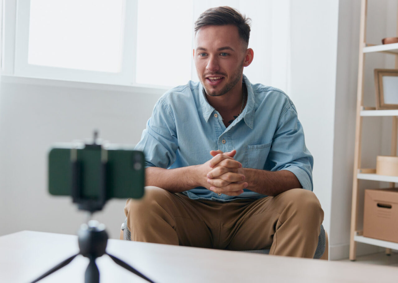 Sociable leader attractive influencer blogger gesticulate recording lesson with phone at home table. Copy space for ad. Electronic IT PC accessories ad. Gadget addiction Online education concept